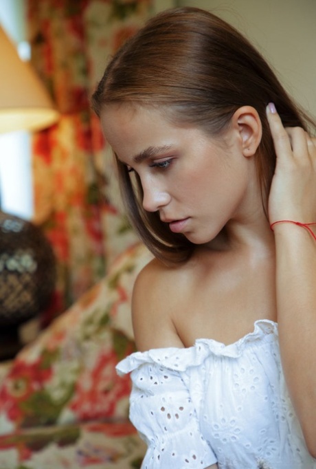 Nice teen Cassia flips thru a book before posing naked on a chesterfield