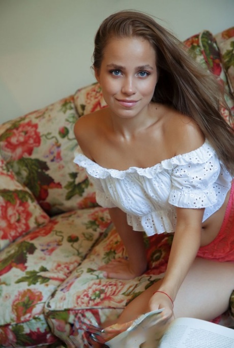 Nice teen Cassia flips thru a book before posing naked on a chesterfield